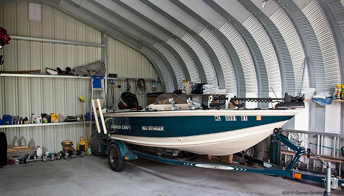 Inside view of a metal building with a blue and white boat parked inside 