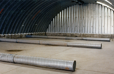 Shows the installation of aerator tubes inside an arch building  that helps to alleviate the build-up of heat during corn storage.