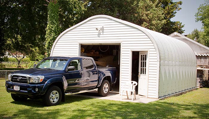 A view of an arch building storing a truck featuring a man door on the front in addition to a garage door 