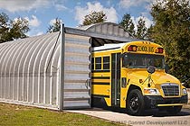 a silver arch building being used as an example for school bus garages featuring a yellow school bus
